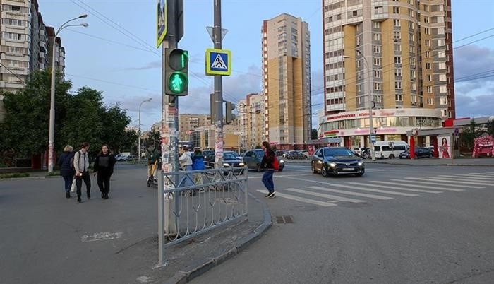 На перекрестке, где встречаются машины и пешеходы, густо толпится транспорт и множество людей.